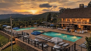 A resort with a swimming pool, lounge chairs, umbrellas, and a building with a balcony overlooking the pool.