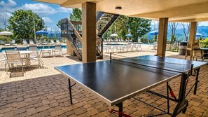 An outdoor pool area with lounge chairs, a ping pong table, and a staircase leading to a covered area. - Chalet Escape | Pet Friendly • Pool • Hot Tub! (Gatlinburg)