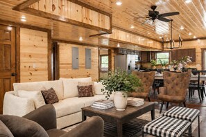 A cozy cabin interior with a wooden ceiling, a sofa, armchairs, a dining table, and a kitchen area. - Cloud's Rest | Luxury Estate • Pool & Pavilion (Sevierville)