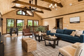 A spacious room with a wooden ceiling, a blue sofa, a coffee table, a fireplace, and a large window. - Cloud's Rest | Luxury Estate • Pool & Pavilion (Sevierville)