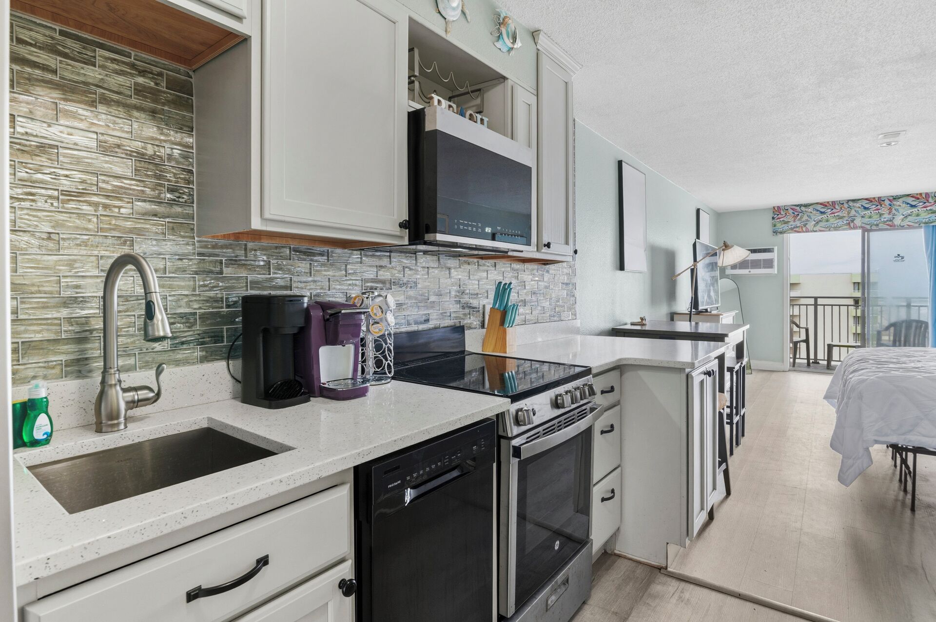 A compact kitchen with a dishwasher, stove, microwave, and a coffee maker.