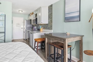 A compact kitchen with a central island, a dining area with stools, and a bed with a quilted cover. - Peaceful 1-bedroom studio with AC in Myrtle Beach (Myrtle Beach)