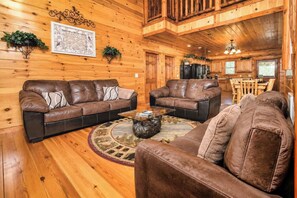 A log cabin interior with two leather sofas, a coffee table, and a dining area with wooden furniture. - Jennie's Cove | 6BR•Private Theater•Indoor Pool! (Sevierville)