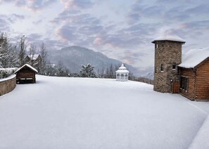 Schneebedeckte Landschaft mit einer Holzhütte, einem Steinturm und einem weißen Gazebo.