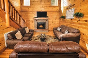 Ein Holzblockhaus-Interieur mit Kamin, Ledersofas und einer Treppe.