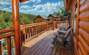 A wooden deck with a railing, wooden benches, and a view of cabins in a forested area. - Jennie's Cove | 6BR•Private Theater•Indoor Pool! (Sevierville)