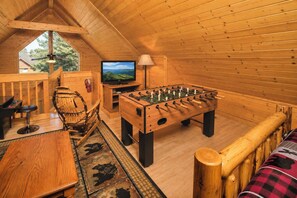Ein gemütliches Zimmer mit Holzwänden, einem Kicker, einem Fernseher und einem Kicker.