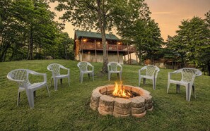 A fire pit with chairs around it, a building in the background, and trees. - Charlie's Creek Retreat | Hot Tub • Game Loft! (Sevierville)
