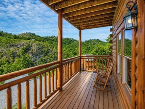 A wooden deck with a railing, a rocking chair, and a view of a forested hillside. - Savannah Splash | Hot Tub • Indoor Pool • Pets OK! (Sevierville)