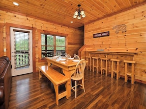 A wooden cabin interior with a dining area, a bench, a bar, and a sign that says 'GATHER HERE'. - Savannah Splash | Hot Tub • Indoor Pool • Pets OK! (Sevierville)