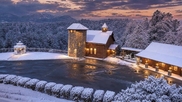 A log cabin with a stone tower, surrounded by snow-covered trees and a frozen lake. - Savannah Splash | Hot Tub • Indoor Pool • Pets OK! (Sevierville)