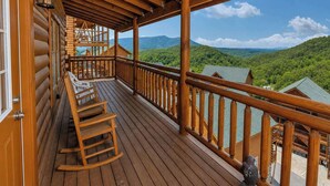 A wooden deck with a railing, a rocking chair, and a view of a forested mountain range. - Savannah Splash | Hot Tub • Indoor Pool • Pets OK! (Sevierville)