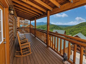 A wooden deck with a railing, a rocking chair, and a view of a forested mountain range. - Savannah Splash | Hot Tub • Indoor Pool • Pets OK! (Sevierville)