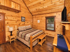 A wooden cabin bedroom with a bed, bedside table, lamp, and a window. - Savannah Splash | Hot Tub • Indoor Pool • Pets OK! (Sevierville)