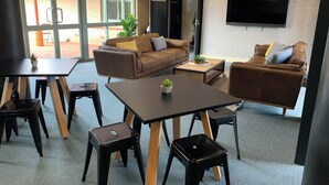 Ein modernes Wohnzimmer mit einer Couch, einem Couchtisch und Sesseln, einem an der Wand befestigten Flachbildfernseher und einem großen Fenster, das für natürliches Licht sorgt.