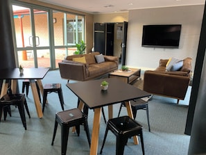A modern living room with a sofa, coffee table, and chairs, a flat-screen TV mounted on the wall, and a large window providing natural light. - Charles Sturt University - CPD Motel (Mitchell)