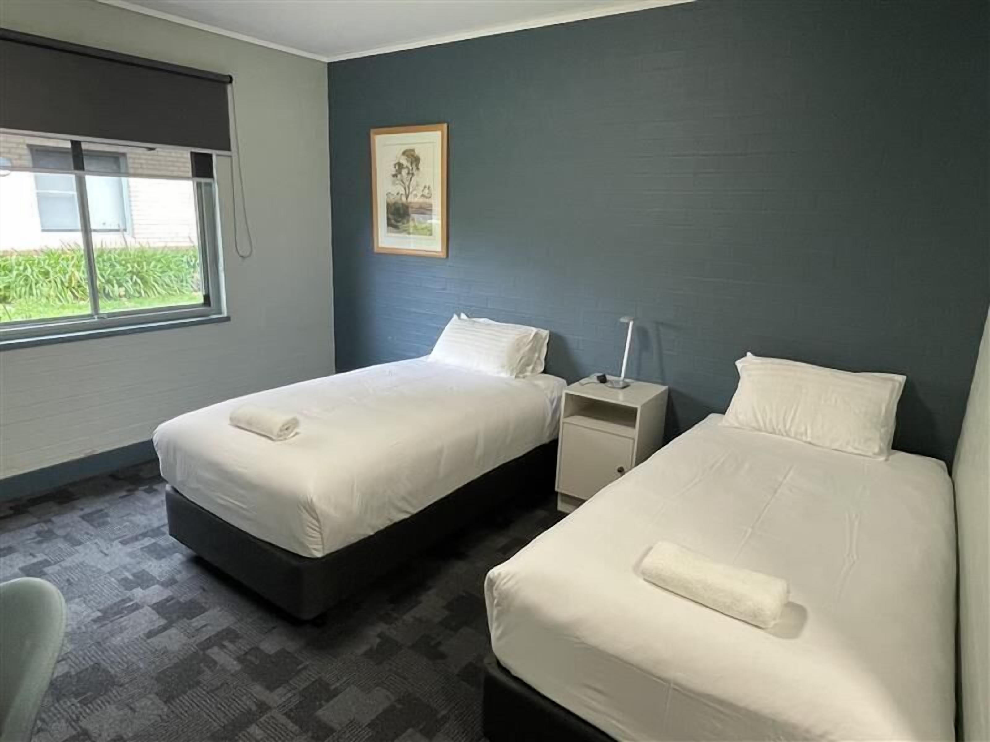 A hotel room with two beds, a window, a nightstand, and a framed picture on the wall.