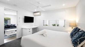 Habitación de hotel con cama, escritorio, televisor, ventilador de techo, aire acondicionado y ventana con vistas.