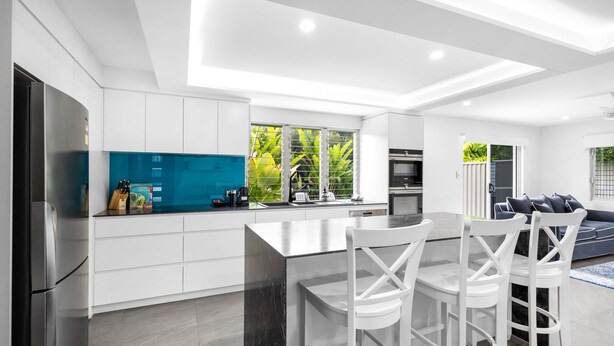 Una cocina moderna con armarios blancos, salpicadero azul y una isla central con sillas.