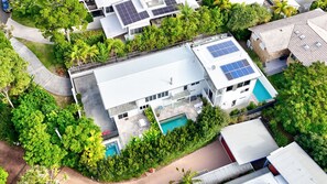 Un moderno edificio residencial con paneles solares, piscina y abundante vegetación.