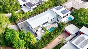 Un edificio moderno de varios pisos con paneles solares, piscina y abundante vegetación.
