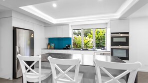 Una cocina moderna con armarios blancos, una isla central, horno empotrado y ventana con vistas al verdor.