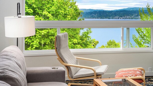 Una sala con vista a un lago y montañas, un sofá, una silla y una mesita.
