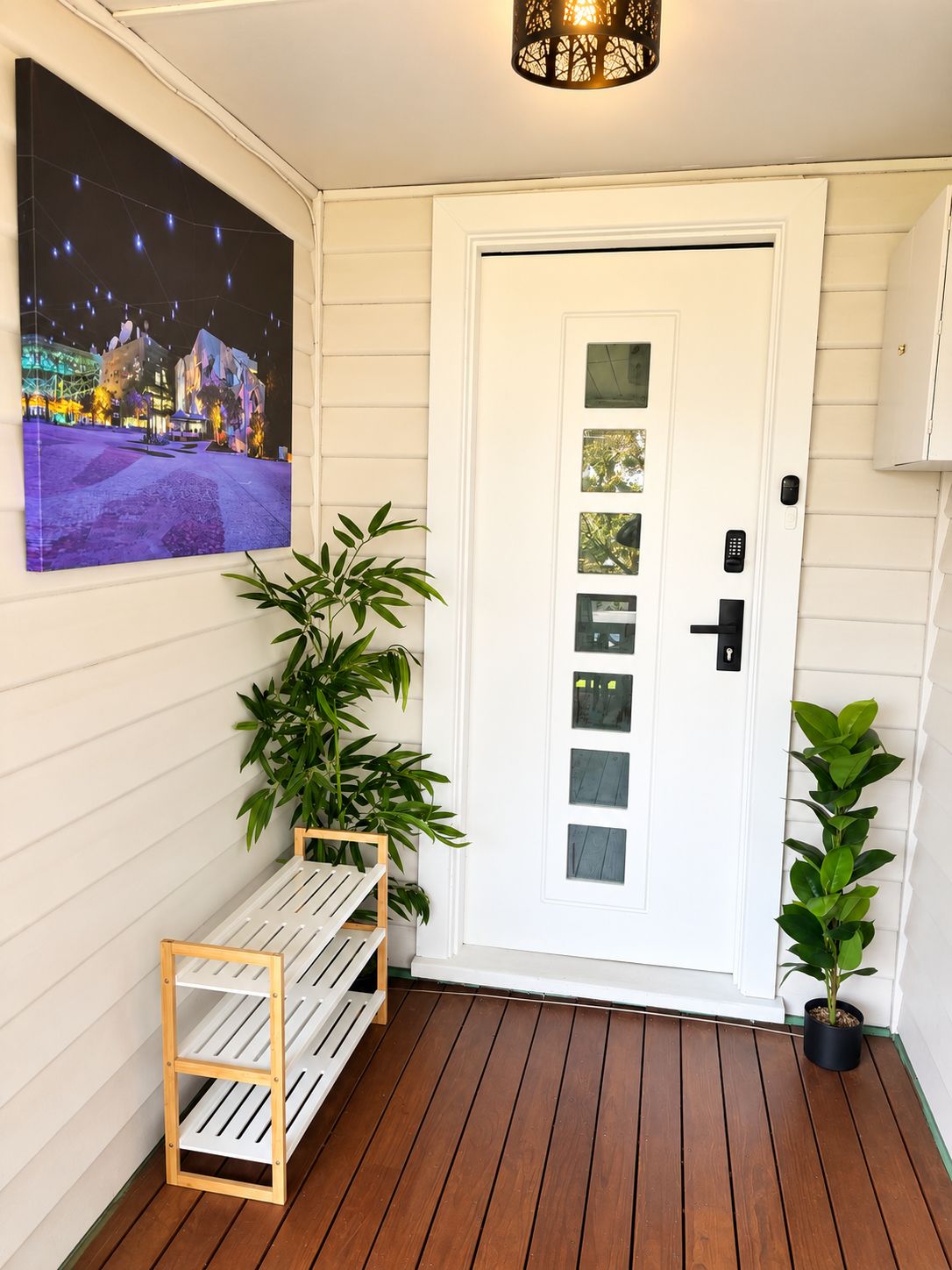 Une porte blanche avec un trou de serrure et une serrure, une petite étagère avec une plante et un tableau encadré accroché au mur.
