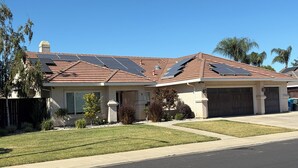 A residential house with a sloped roof, solar panels, a garage, and a well-maintained lawn.