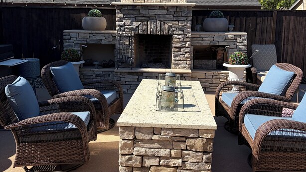 A stone fireplace with a chimney, outdoor wicker furniture, and a concrete table.