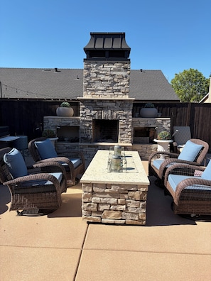 A stone fireplace with a chimney, outdoor wicker furniture, and a concrete table. - Private Pool, Spa & Extended-Stay Ready! Where comfort meets convenience. (Colusa)