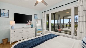 Quarto com cama, televisão, penteadeira e uma janela grande com vista.
