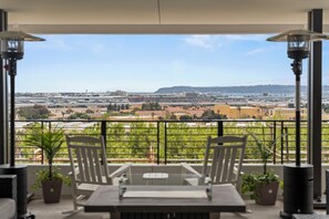 Ein Balkon mit Tisch und Stühlen, Blumentöpfen und Blick auf einen Flughafen.