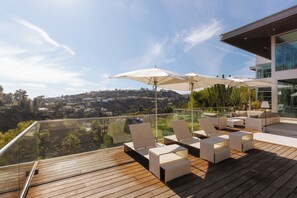 A modern outdoor deck with glass balustrades, white cushioned seating, and large umbrellas. - Hollywood Hills Private Oasis with amazing views (Los Angeles)