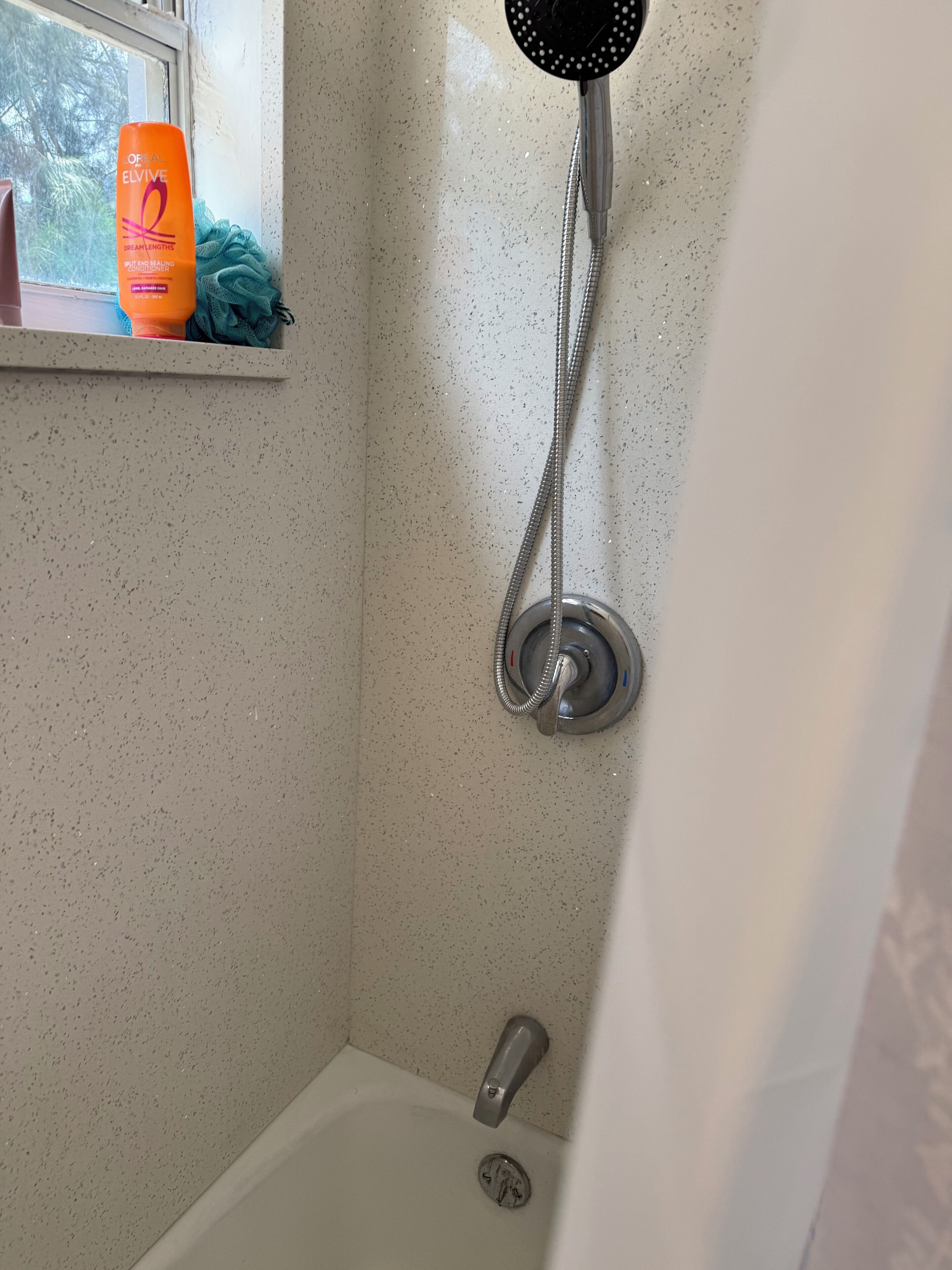 A bathroom with a shower, a window with a shelf holding toiletries, and a bathtub.