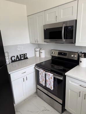 A modern kitchen with white cabinets, a stainless steel microwave, an oven, and a coffee maker.