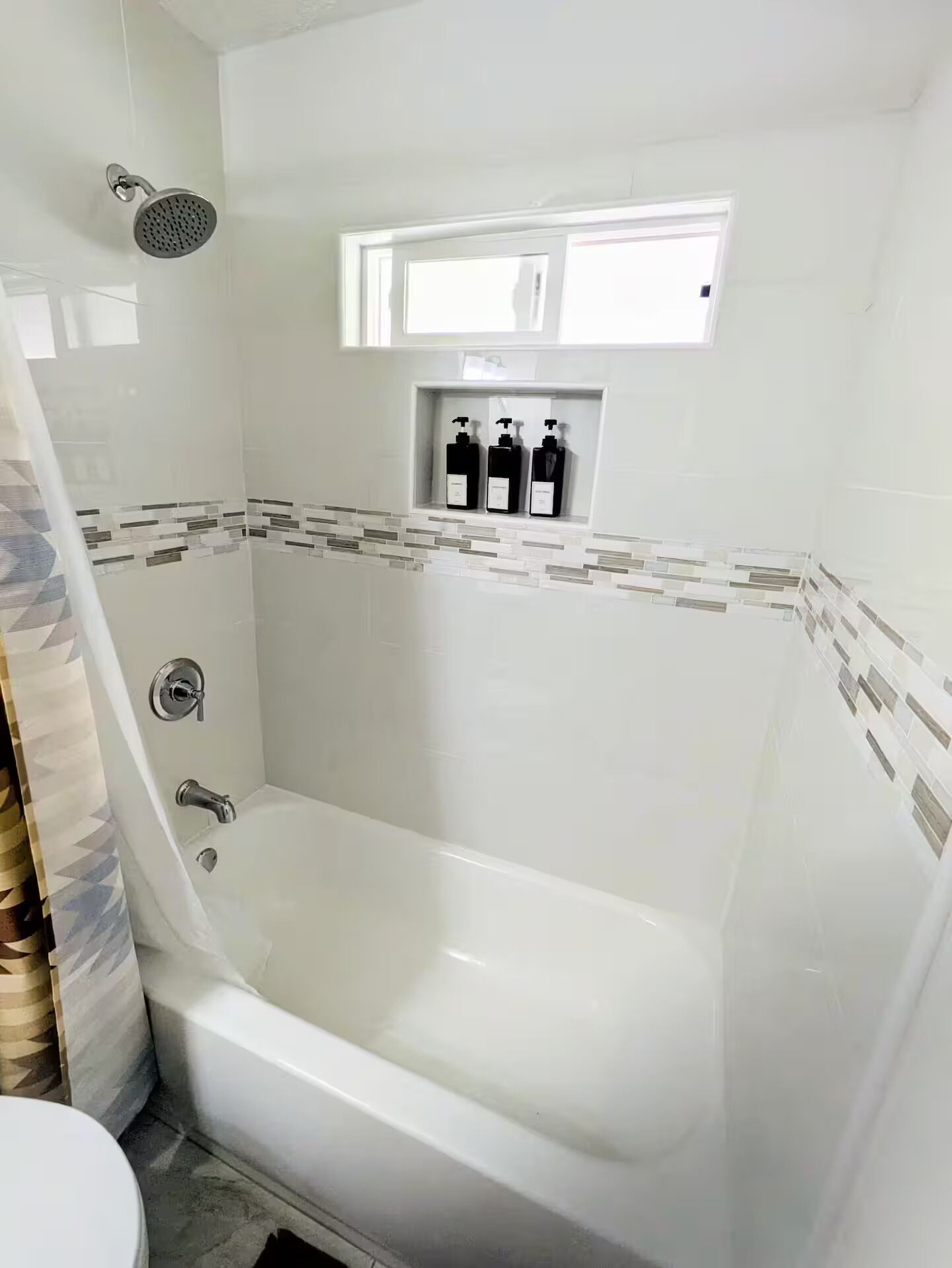 A bathroom with a bathtub, shower, and a shelf with toiletries.
