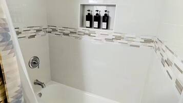 A bathroom with a bathtub, shower, and a shelf with toiletries.