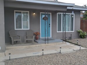 A residential house with a front porch, two chairs, a potted plant, and a blue door.