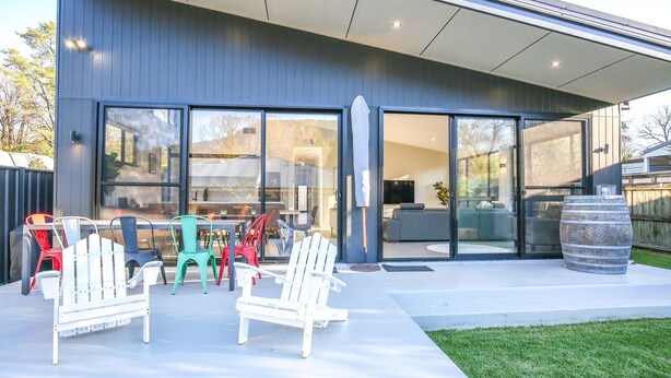 Une maison moderne dotée de grandes portes-fenêtres coulissantes, d’un patio avec mobilier d’extérieur et d’une grande cuve.
