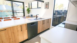 Eine moderne Küche mit Holzausstattung, Geschirrspüler, Spüle und einem Essbereich mit Stühlen.