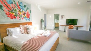 Une chambre d’hôtel avec un lit, une chaise, un bureau, un miroir et des œuvres d’art accrochées au mur.