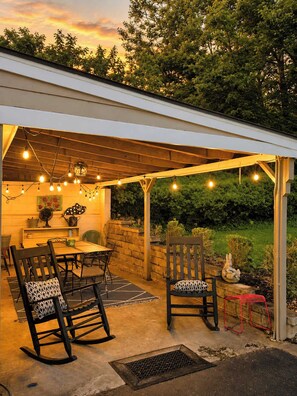 Eine Terrasse im Freien mit Tisch, Stühlen, Lichterkette und Blick auf einen Garten.