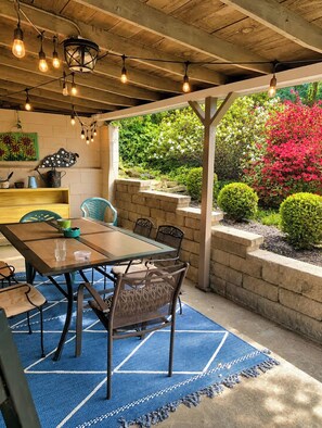 An outdoor patio with a wooden table and chairs, surrounded by a stone wall and lush greenery. - Fully Renovated 1950s Urban Chic Deer Park Retreat (Louisville)