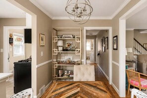 A hallway with a built-in bookshelf, a tufted chair, and a herringbone-patterned floor. - Fully Renovated 1950s Urban Chic Deer Park Retreat (Louisville)