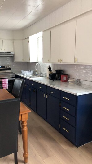 A kitchen with white cabinets, a marble countertop, and a dining area with a wooden table and chairs. - The Downtown Hamilton House (Shédiac)