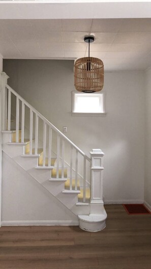 A staircase with white railings and yellow steps, a woven pendant light, and a small window. - The Downtown Hamilton House (Shédiac)