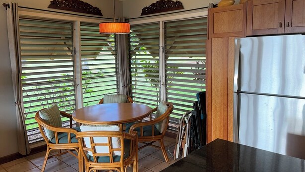 A kitchen with a dining table, chairs, a hanging light fixture, and a refrigerator.