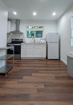 Eine kleine Küche mit weißen Schränken, einer Edelstahl-Dunstabzugshaube, einem Backofen und einem Kühlschrank.