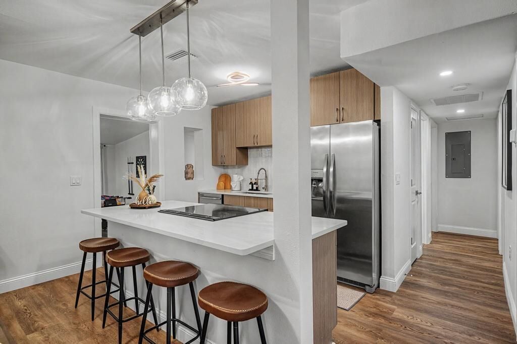 A modern kitchen with a central island, bar stools, stainless steel appliances, and pendant lighting.